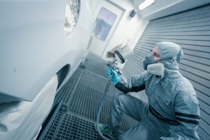 Mitarbeiter in Schutzkleidung lackiert Fahrzeug mit Spritzpistole